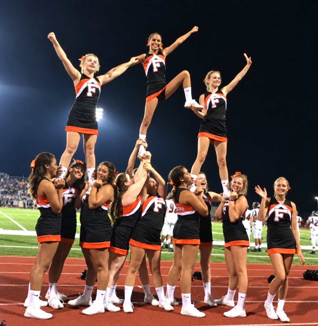 School cheer squad performing a stunt pyramid at a night football game